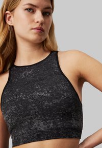 Top sportivo corto nero con tessuto testurizzato, scollatura alta e design racerback. Presenta un logo discreto sul fronte.