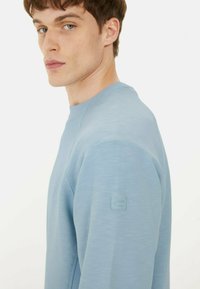 Helles Blaues Sweatshirt mit strukturiertem Finish, Rundhalsausschnitt und gerippten Akzenten an den Schultern. Mit einem dezenten Logo auf dem linken Ärmel.