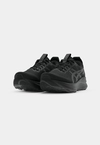 Baskets de sport noires avec un dessus texturé, une semelle rembourrée et un logo distinctif sur le côté. Comprend une sangle de traction et un design à lacets.