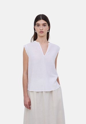 Top de lino blanco con mangas cortas y escote en forma de V. Presenta bordes de mangas en forma de ondas y un corte relajado. Textura suave. Color claro.
