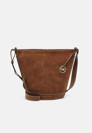 Sac bourse en cuir marron avec bandoulière réglable, coutures blanches, et un pendentif rond en or avec le logo Michael Kors sur un fond uni.