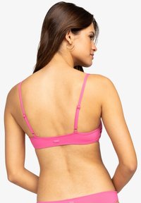Top de bikini rosa con tirantes ajustables, textura suave y un logo en la banda trasera, diseñado para un ajuste ceñido.