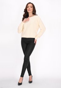 Top a maniche lunghe color crema con una vestibilità rilassata, abbinato a leggings neri aderenti e scarpe con il tacco nere. Texture liscia.
