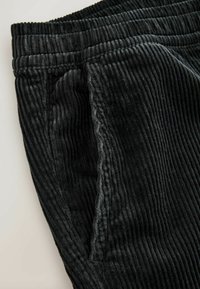 Black corduroy pants featuring a ribbed texture, elastic waistband, and side pockets. Close-up of fabric detail and stitching visible.