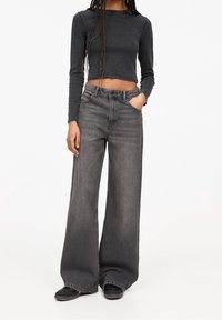 Chemise crop top à manches longues gris foncé associée à un jean denim gris à jambes larges. Le jean présente une texture légèrement délavée et des poches avant.