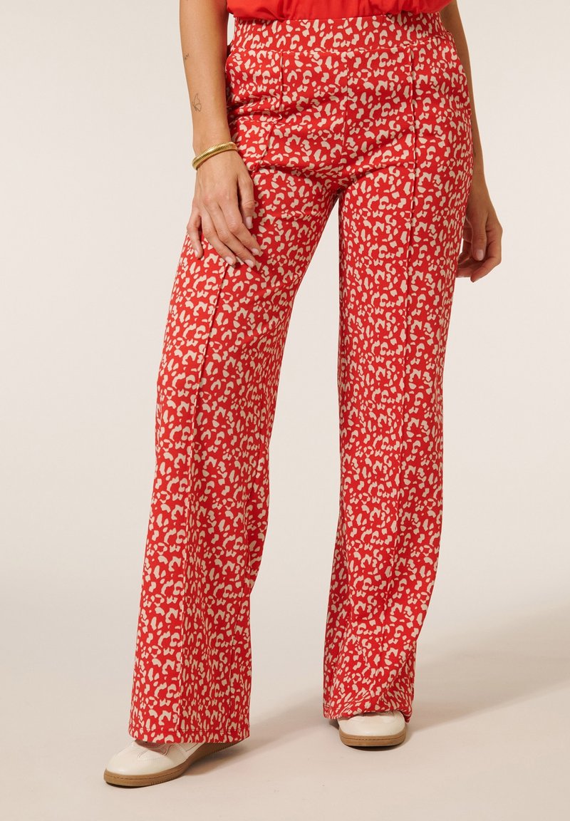 Rode gestreepte broek met een witte abstracte dierenprint, rechtlopende pasvorm en subtiele textuur. Gecombineerd met een effen top en schoenen.