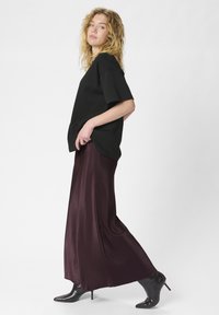 Schwarz oversized T-Shirt mit kurzen Ärmeln kombiniert mit einem langen, tiefburgunderfarbenen Satinrock. Schwarze spitze Absatzschuhe runden das Outfit ab.