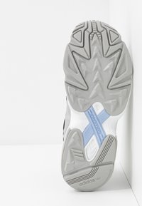 Grå och vit sportskosula med texturerade mönster, blå detaljer i mellansulan och framträdande mönsterdesign för grepp och stöd.