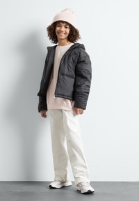 Sort puffjakke med hætte, lange ærmer og lynlås, båret over en lys pink sweatshirt og cremede, vide bukser.