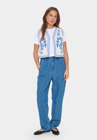 Vit väst med blåblommig broderi, tillsammans med en vit t-shirt och högmidjade jeans. Svarta platta skor fulländar looken.