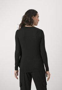 Top nero a maniche lunghe con scollatura rotonda, design aderente e texture liscia. Sul retro presenta dettagli di cuciture sottili e una silhouette snella.