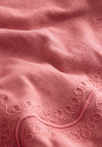 Rosa gefärbter Stoff mit weicher Textur, der an einer Kante zarte gestickte Schlaufen in einem kontrastierenden Faden aufweist.