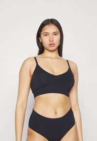 Svart bralette med tynne stropper og V-halsdesign, kombinert med høyt liv, sømløs svart undertøy laget av myk, elastisk stoff.