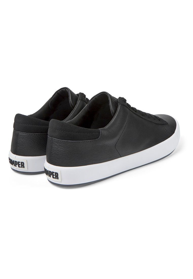 Zapatillas de cuero negro con textura suave, diseño de corte bajo, suelas de goma blanca y una marca sutil en el talón. Sin patrones visibles.