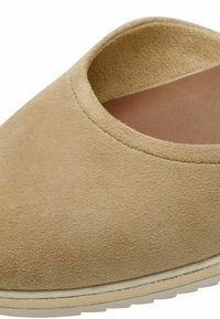 Zapato sin cordones de ante beige con puntera redondeada y una suela de goma texturizada baja. Cuenta con un interior suave y liso y costuras mínimas.
