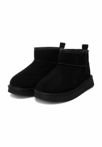 Botines de ante negro con punta redonda, suela de goma plana y acentos de costura. Presentan tiradores para facilitar su uso.