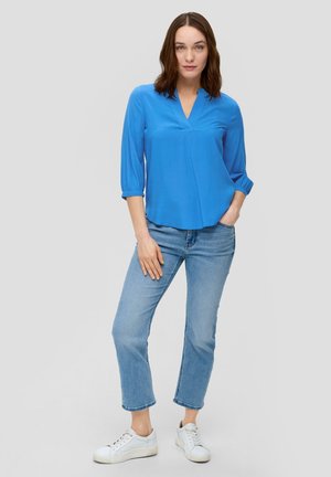 Lichtblauwe, luchtige blouse met een V-hals en driekwart mouwen, gecombineerd met lichtkleurige spijkerbroek en witte sneakers.