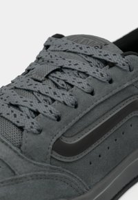 Sneaker in suede grigia con superficie texturizzata, lacci grigi scuri, suola in gomma e dettagli a striscia laterale. Perforazioni per la ventilazione vicino alla suola.