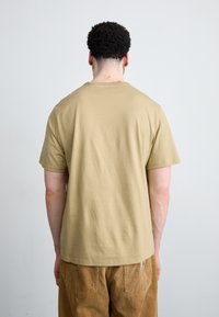 Tan katoenen t-shirt met korte mouwen, ruime pasvorm en ronde halslijn, gecombineerd met corduroy broek in een bijpassende kleur, gezien van achteren.