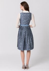 Blaues, blumenmusterndes Kleid mit einem plissierten Rock und einem hellblauen Gürtel. Der obere Teil hat einen taillierten Schnitt mit einer weißen, langärmligen Bluse aus Spitze.
