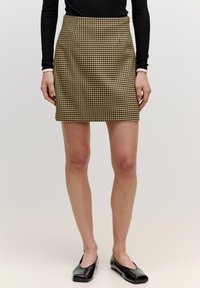 Braun-beige kariertes Minirock mit tailliertem Schnitt, der eine glatte Textur und einen Reißverschluss auf der Rückseite aufweist. Kombiniert mit schwarzen Ballerinas.