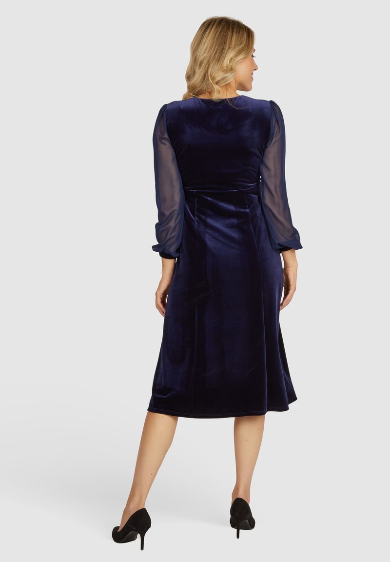 Navy Samtkleid mit transparenten langen Ärmeln; mittellange Silhouette; taillierter Oberteil; fließender Rock; Rückansicht, die die glatte Textur und das elegante Design zeigt.