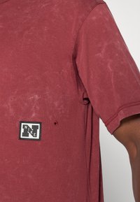 Camiseta de manga corta color marrón, hecha de algodón texturizado, con un parche del logo de Nike en blanco y negro en el pecho izquierdo.