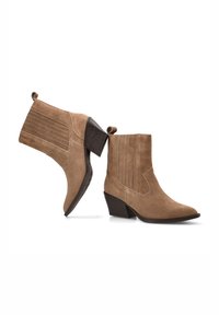 Botas de tobillo de ante color marrón claro con punta afilada, tacón curvado y detalles de costura vertical en los laterales. Detalle de bucle en la parte superior para facilitar su uso.