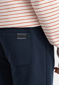 Marine joggingsbroek met een gestikte zak, voorzien van een zwart label op de tailleband. Het bovenstuk heeft rode strepen op een witte achtergrond.
