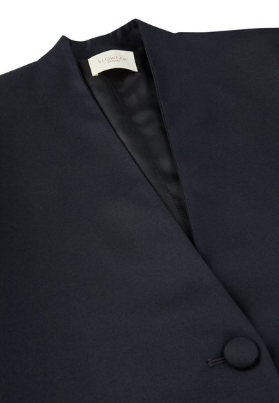 Granatowa kamizelka o minimalistycznym designie, z zapięciem na guzik i gładką, matową fakturą. Etykieta widoczna wewnątrz.