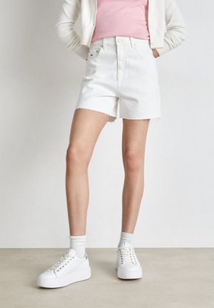 Bermudas de mezclilla blancas con dobladillo desflecado y cintura alta, combinadas con zapatillas blancas y calcetas. El conjunto se complementa con una blusa rosa y un cárdigan ligero.