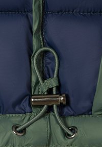 Nahaufnahme von marineblauem und grünem Stoff mit einer grünen Kordelschlaufe, die mit einem silbernen Metallschieber gesichert ist.