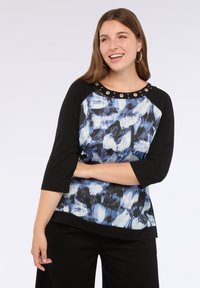 Top nero e blu con un motivo astratto testurizzato, maniche a tre quarti e dettagli circolari sullo scollo. Vestibilità leggermente larga.
