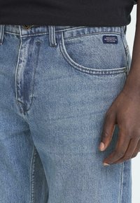 Ljusblå denimjeans med rak passform, som har klassiska fickor, knappstängning och en liten märkesetikett på midjebandet.
