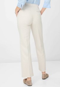 Beige gemusterte Hosen mit schmalem Bund, Gesäßtaschen und geraden Beinen. Getragen mit einem hellblauen Oberteil und braunen Schuhen.