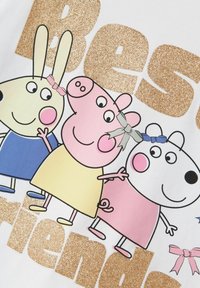 Marškinėliai su animacinių filmų gyvūnais: geltonas triušis, rožinis kiaulė ir baltas šuo, su rožinėmis ir mėlynomis kaspinais, ir blizgančiu auksiniu „Geriausi draugai“ tekstu.