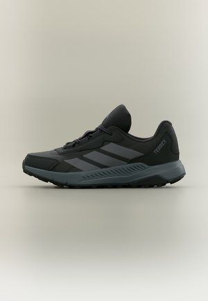 Zwarte en donkergrijze Adidas Terrex trail hardloopschoen met vetersluiting en een textuurzool, zijaanzicht op een neutrale achtergrond.
