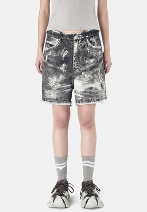 Persoon draagt zwart-witte acid-washed denim shorts met rafelige zoom, grijze sokken met witte strepen en zwart-witte sneakers.