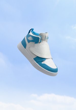 Hvid og blå højt sneaker med en tekstureret klap over snørebåndene, svævende mod en klar blå himmel baggrund.