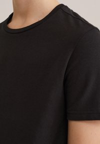 Juoda medvilninė marškinėliai su apvalia iškirpte ir trumpomis rankovėmis, pasižymintys lygiu paviršiumi ir švariu, paprastu dizainu.