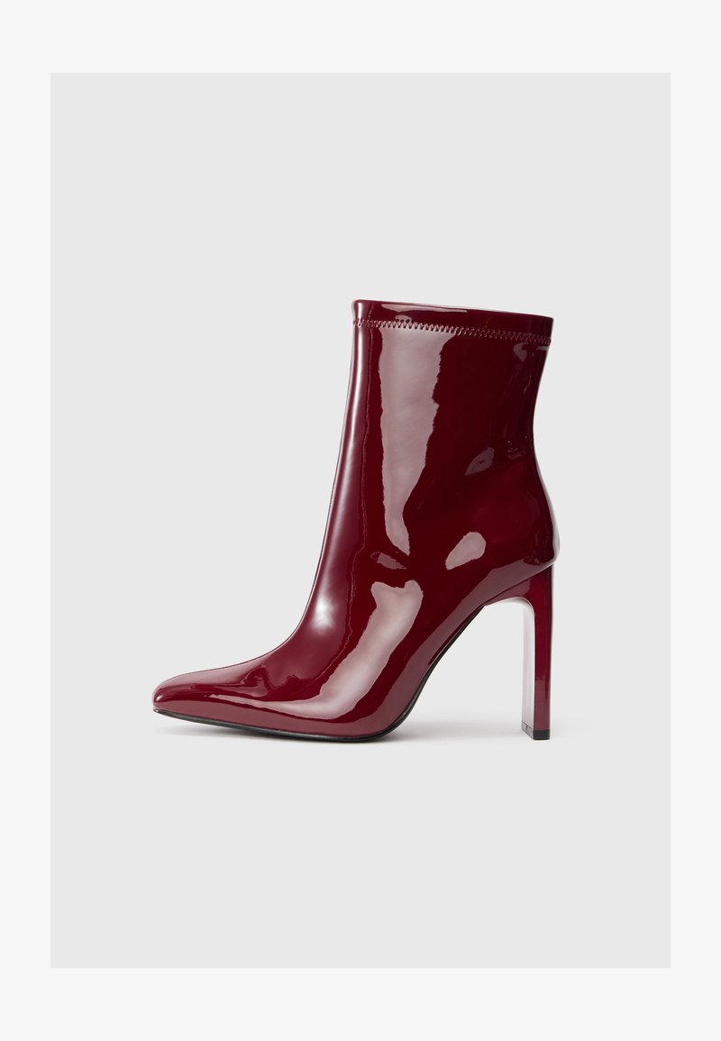 Bota de tornozelo em pele patinada cor burgundy com bico fino e alto salto stiletto. Textura suave com um detalhe discreto na parte superior.