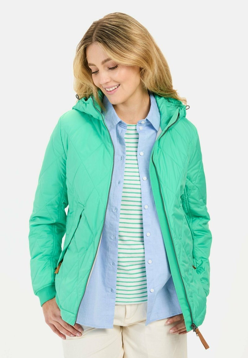 Gequilted groene jas met capuchon, ritssluiting en zijzakken. Draag over een lichtblauwe button-up shirt en een groen-wit gestreept shirt.