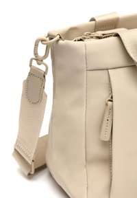 Beige texturerad handväska i mjukt material, med avtagbar rem, metallbeslag och sydda detaljer på kroppen och remmen.