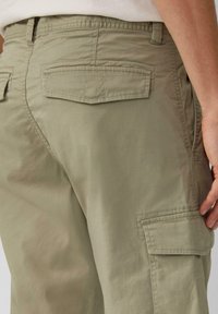 Pantalons cargo verts olive en coton. Dispose de deux poches arrière et d'une poche latérale, avec une texture lisse et un design utilitaire.