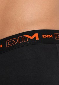 Mustat puuvillaboksarit, joissa on musta joustava vyötärönauha, jossa on oranssi "DIM"-logo. Silkkinen pinta ja muotoilultaan kireät.