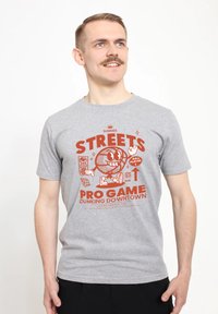 Šedé bavlněné tričko s krátkým rukávem, které na přední straně obsahuje barevný potisk s textem, grafickými postavami a prvky spojenými se sportem.