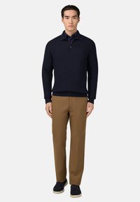 Námořnický pletený svetr s ribbovanou texturou, límcem a knoflíkovou légou se třemi knoflíky, doplněný o hnědé kalhoty s rovnými nohavicemi a tmavé boty.