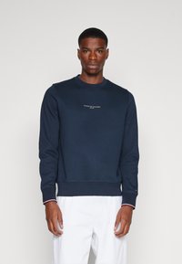 Felpa blu navy realizzata in un materiale morbido, con collo a giro e polsini a costine con accenti rossi e bianchi, e un piccolo logo sul petto.
