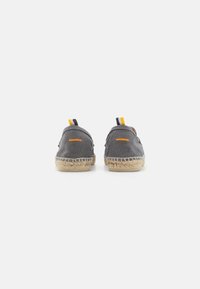 Grå canvas espadriller med en naturlig jutesål, der har gule og marineblå stribede detaljer ved hælen samt enkle syninger.