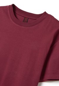 Camicia corta bordeaux, in morbido cotone, con collo a giro e design semplice, presenta un piccolo etichetta nera e rossa sul colletto.